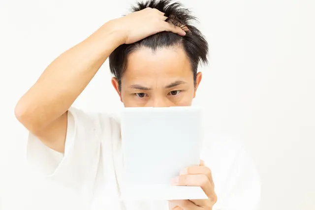 鏡で眉毛をチェックする男性